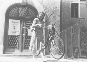 Die Assistentin Dr. Irmgard Meßtorff vor dem Eingang des Gebäudes Boltzmannstraße 20 beim Transport von Gerät für die Experimentalphysik-Vorlesung; Sommer 1949. Das Fahrrad war wichtiges Transportmittel.